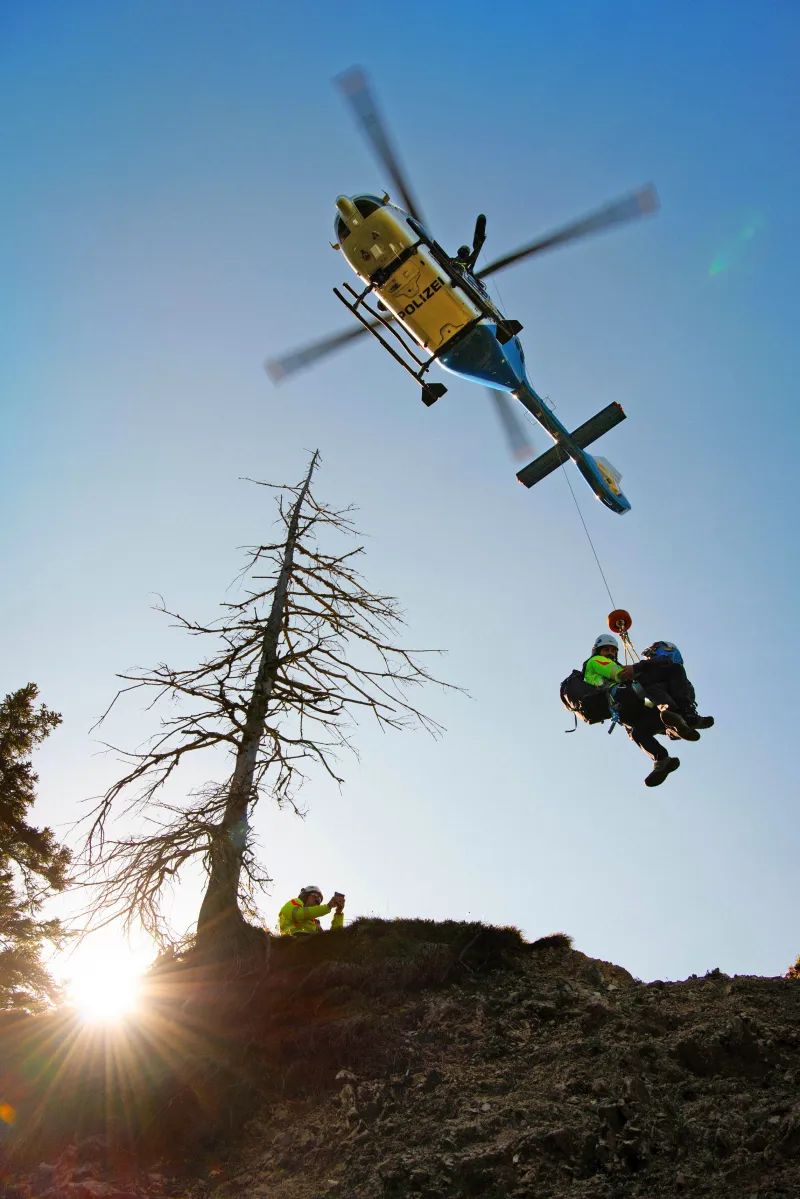 Hubschrauber mit zwei Personen am Seil während eines Bergungseinsatzes.