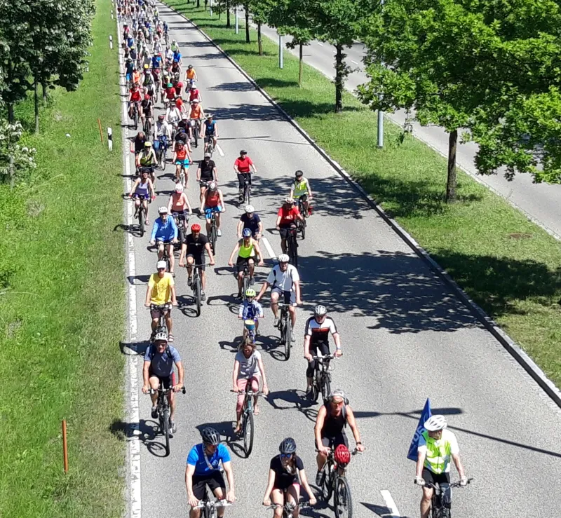 Teilnehmer einer Radveranstaltung fahren im Sommer eine Straße entlang.
