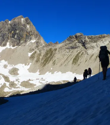 Wanderer auf einer Bergtour über einen teils verschneiten Gipfel.