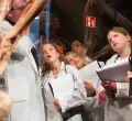 Kinder in Arztkitteln, die staunend einen menschlichen Körper betrachten.