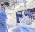 Ein Arzt in steriler blauer Kleidung bei der Arbeit, im Hintergrund sind Monitore