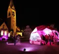 Der Sankt-Mang Platz bei Nacht, mit beleuchteter Kirche und einem pink beleuchteten KunstNacht Zelt im Vordergrund