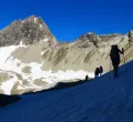 Wanderer auf einer Bergtour über einen teils verschneiten Gipfel.
