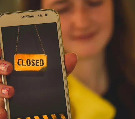 Ein Mädchen dass ein Handy in die Kamera hält auf dem "Closed" steht