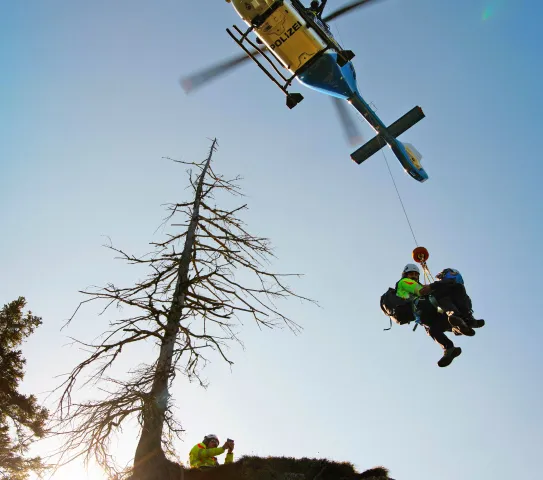 Hubschrauber mit zwei Personen am Seil während eines Bergungseinsatzes.