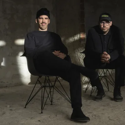 Die Gründer Tom (links) und Philipp Herzhoff in einem Rohbau-Raum ganz in schwarz gekleidet und sitzend.