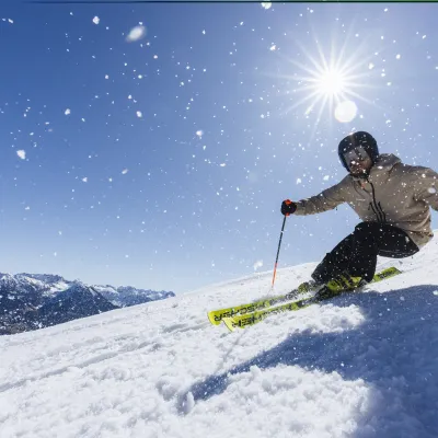 Skifahrer auf Pistenabfahrt bei strahlend blauem Himmel.